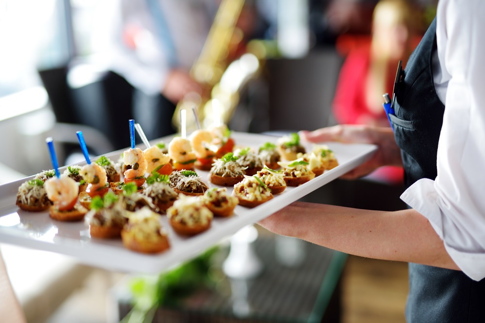 A vibrant office party with an assortment of gourmet finger foods, desserts, and beverages displayed on a decorated table.