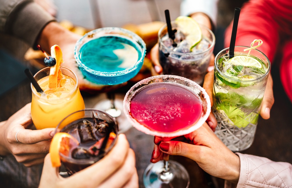 A vibrant office party with an assortment of gourmet finger foods, desserts, and beverages displayed on a decorated table.